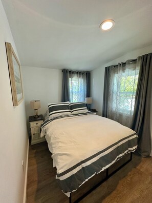 Een slaapkamer met een bed, twee nachtkastjes, een lampje, een raam met gordijnen en een plafondlamp.