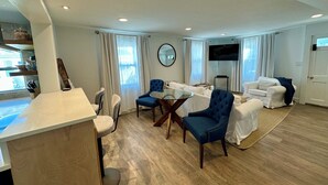 A modern living room with a dining area, a flat-screen TV, and a large window with curtains. - Charming 3-bedroom beach cottage in beautiful Fairfield with AC (Fairfield)