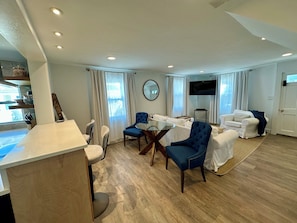 Een moderne woonkamer met een eethoek, een flatscreen televisie en een groot raam met gordijnen.