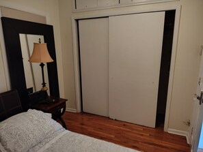 A bedroom with a bed, a nightstand, a lamp, a wardrobe, and a door.