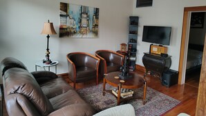 A living room with a sofa, two armchairs, a coffee table, a painting, a lamp, a TV, and a bookshelf. - Enjoyable 1-bedroom apartmen
t with AC in vibrant Brooklyn (Brooklyn)