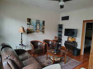 A living room with a sofa, two armchairs, a coffee table, a painting, a lamp, a TV, and a bookshelf.