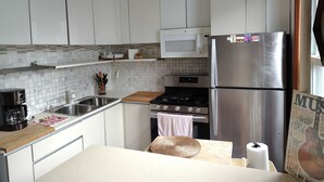 A kitchen with white cabinets, a stainless steel refrigerator, a microwave, a stove, and a coffee maker. - Enjoyable 1-bedroom apartmen
t with AC in vibrant Brooklyn (Brooklyn)