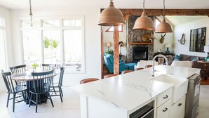 Een moderne keuken met een marmeren kookeiland, hanglampen en een stenen open haard.