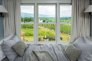 Un dormitorio con un ventanal grande, una cama con ropa de cama gris y vistas a un viñedo.