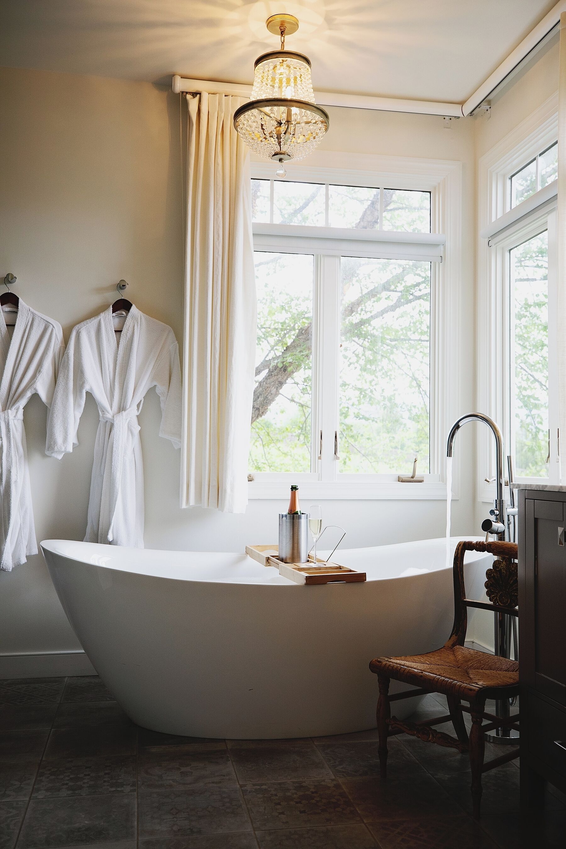 A bathroom with a freestanding bathtub, a wooden chair, and two white bathrobes hanging on a rack.