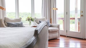 Ett sovrum med en säng, en soffa, ett litet bord med en vas och utsikt genom en glasdörr.