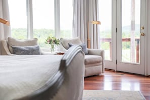 Une chambre à coucher avec un lit, un canapé, une petite table sur laquelle est posé un vase, et une vue à travers une porte vitrée.