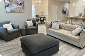 Ein Wohnzimmer mit einer Couch, zwei Sesseln, einem Couchtisch und einem Essbereich mit Tisch und Stühlen.