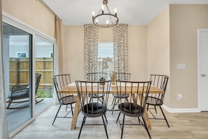 A dining area with a wooden table and black chairs, a chandelier, and a view of a backyard through a sliding glass door.