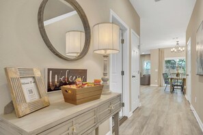 A hallway with a wooden console table, a mirror, a lamp, a welcome sign, and a QR code. - Luxury Jax Beach House: Walk to Beach, Game Room & Backyard with Firepit (Jacksonville Beach)