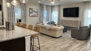 Un salon moderne avec un canapé, des fauteuils, un téléviseur et un ventilateur de plafond.