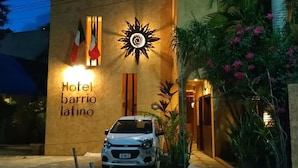 Een gebouw met een bord waarop 'Hotel barrio latino' staat, een geparkeerde auto en een zonachtige decoratie.