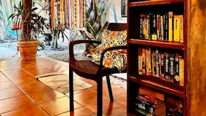 Een kamer met rieten dak, een boekenkast vol boeken, een stoel en een kamerplant.