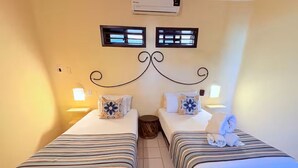 Twee enkele bedden met gestreept beddengoed, een wandairconditioner en twee wandlampen.