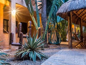 Un jardin tropical doté d’une structure à toit de chaume, de palmiers et d’un espace détente avec des chaises.