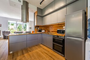 A modern kitchen with grey cabinets, a stainless steel refrigerator, a built-in oven, and a wooden countertop. - Coastal Bloom Villa Garden BBQ (Ishëm)