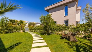 A modern building with a well-maintained lawn, a stone pathway, and outdoor furniture. - Coastal Bloom Villa Garden BBQ (Ishëm)