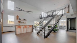 A spacious kitchen with a central island, a staircase with a metal railing, and a view of the city through large windows. - Prime SLC - Airport - Convention - Hot tub (Salt Lake City)