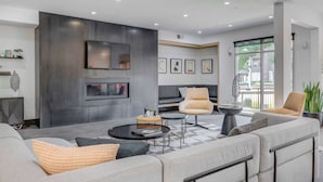 A modern living room with a sofa set, a coffee table, and two armchairs. There is a flat-screen TV mounted on the wall, and a fireplace below it. - Prime SLC - Airport - Convention - Hot tub (Salt Lake City)