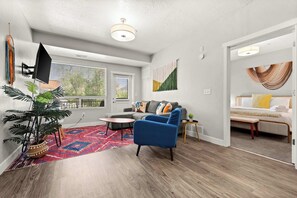 A modern living room with a sofa, a blue armchair, a coffee table, a potted plant, and a red and blue rug.