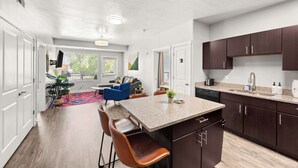 A modern kitchen with a central island, dark wooden cabinets, and a dining area with a blue chair.
