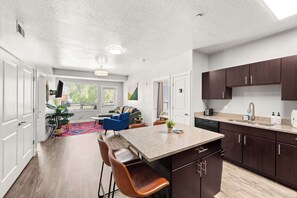 Une cuisine moderne dotée d’un îlot central, de meubles de rangement en bois foncé et d’un coin repas avec une chaise bleue.