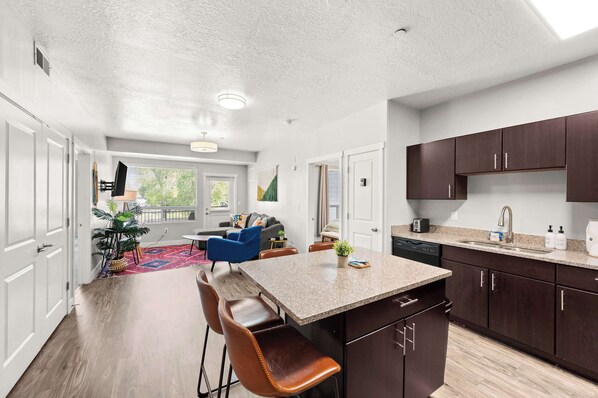 A modern kitchen with a central island, dark wooden cabinets, and a dining area with a blue chair.