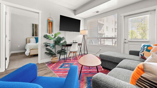 A modern living room with a flat-screen TV, a blue sofa, a grey sofa, a small round table, and a colorful rug.