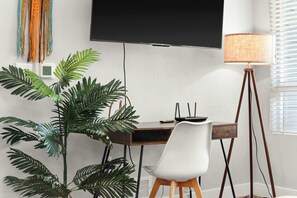 Um espaço de escritório moderno com escrivaninha, cadeira, planta grande, abajur e uma TV de tela plana fixada na parede.