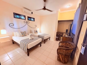 A hotel room with two beds, a ceiling fan, a small table with a chair, and a window with blinds.