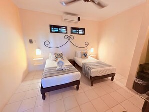 Ein Schlafzimmer mit zwei Betten, einem Deckenventilator, einer Klimaanlage und einem kleinen Fenster mit Rollläden.