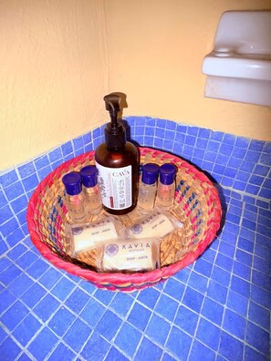 Une salle de bain avec un sol carrelé de carreaux bleus, un panier en osier contenant des articles de toilette et une bouteille de savon d’hôtel de la marque CAVA.