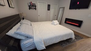 Ein Schlafzimmer mit einem Bett, einem an der Wand montierten Fernseher, einem Kamin und einer Tür.