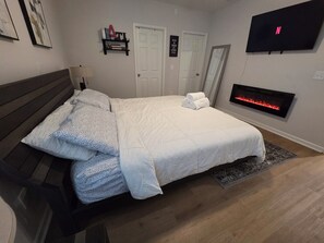 Ein Schlafzimmer mit einem Bett, einem an der Wand montierten Fernseher, einem Kamin und einer Tür.