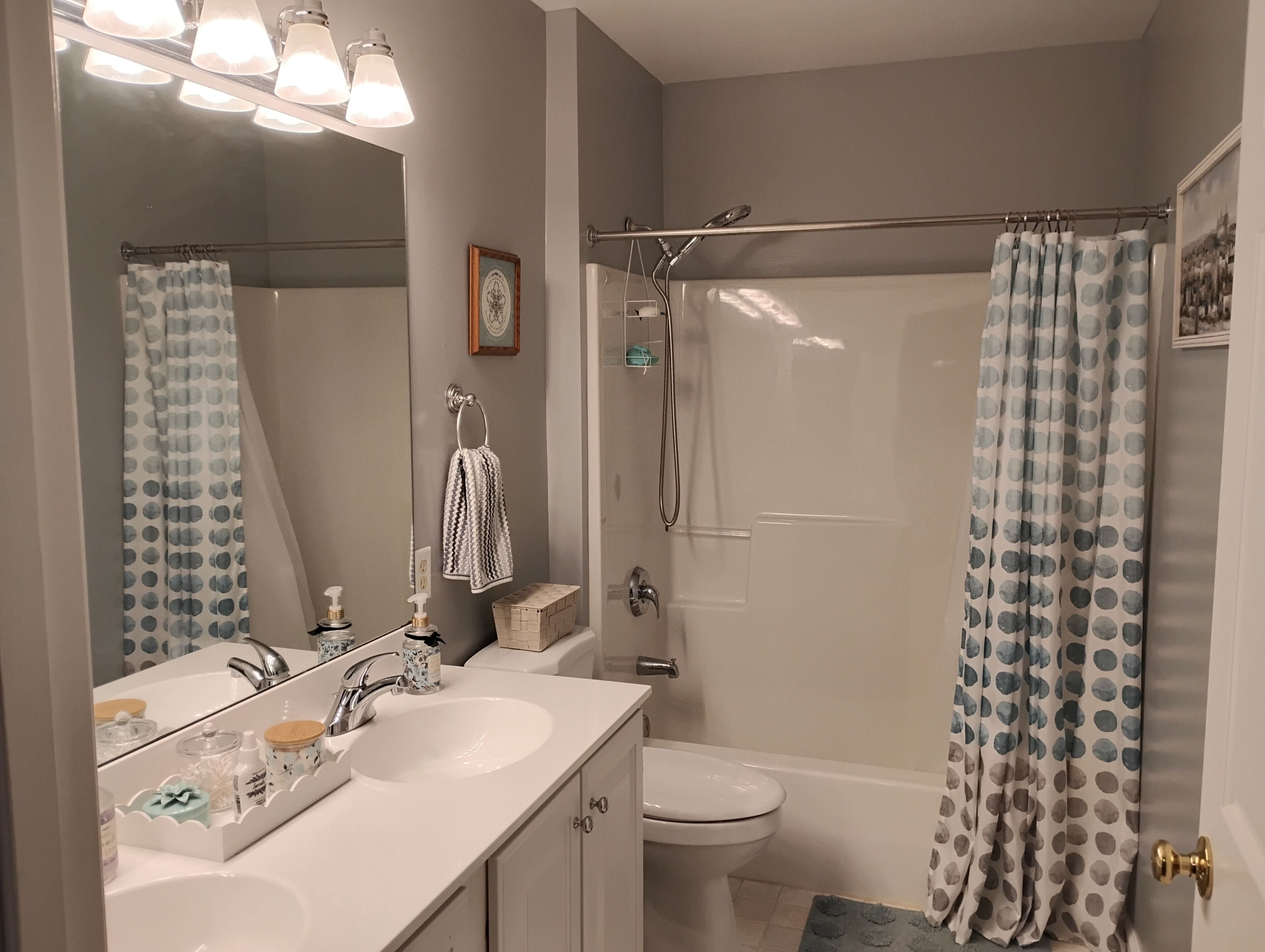 A bathroom with a white sink, a toilet, a shower with a curtain, and a mirror with lights above.