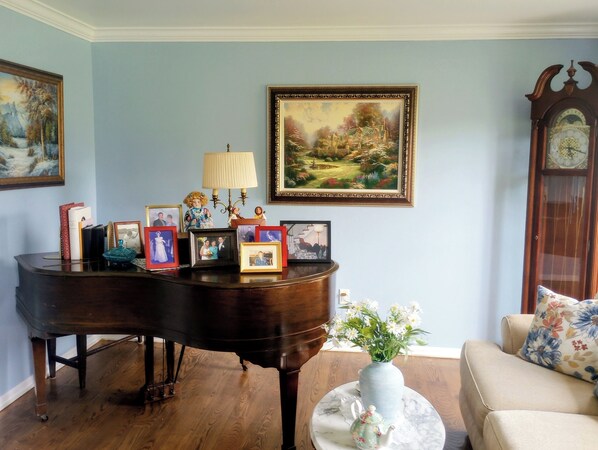 Una habitación con un piano de cola, un florero con flores, cuadros enmarcados y un cuadro en la pared.