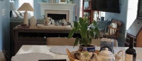 Un coin repas avec une table dressée pour deux personnes, une pancarte indiquant « Bienvenue à vos amis et à votre famille », une bouteille de vin et un téléviseur en arrière-plan.