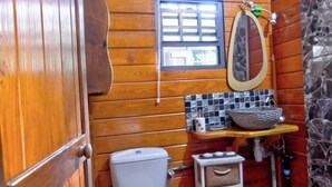 A compact bathroom with wooden walls, a white toilet, a small window, a mirror, and a sink with a stone basin. - Cozy cottage "Cocotier" w/pool in the complex (Cul de Sac)