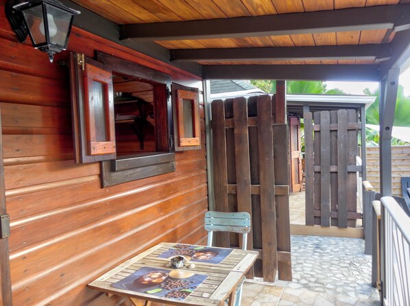 A wooden exterior with a covered patio area, a table with a coffee-themed placemat, and a wooden fence.
