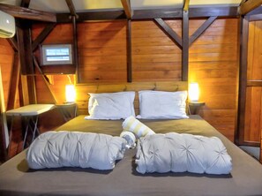 A wooden-paneled room with a bed, two bedside tables, and two wall-mounted lamps.