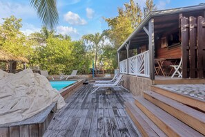Une terrasse en bois avec des chaises longues, une piscine et un espace couvert équipé de tables et de chaises.