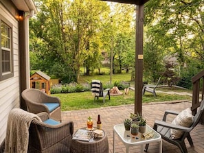 Eine überdachte Terrasse mit Korbmöbeln, einem kleinen Tisch mit Getränken und Blumentöpfen.