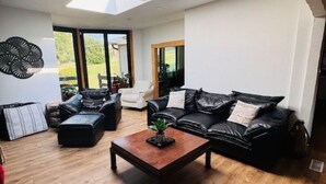 A modern living room with a wooden floor, a black leather sofa, a wooden coffee table, and a skylight.