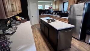 A modern kitchen with wooden cabinets, a stainless steel refrigerator, and a large island with a sink.