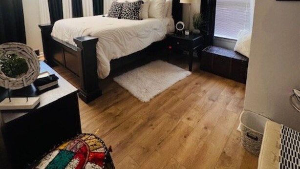 A bedroom with a bed, bedside tables, a lamp, a window with curtains, a rug, and a small stool.