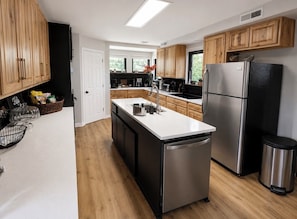 A modern kitchen with wooden cabinets, stainless steel appliances, and a central island. - Dallas Cowboys Farmhouse Retreat • Sleeps 10 • By AT&T Stadium (Grand Prairie)