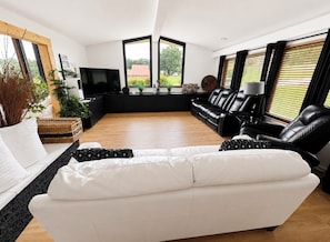 A modern living room with a white sofa, black leather chairs, a flat-screen TV, and large windows with blinds. - Dallas Cowboys Farmhouse Retreat • Sleeps 10 • By AT&T Stadium (Grand Prairie)
