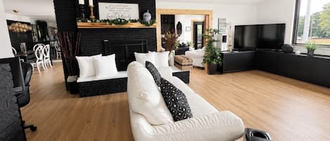 A modern living room with a fireplace, white sofas, a flat-screen TV, and a wooden floor.