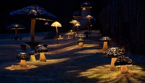 A pathway lined with mushroom-shaped structures, some with umbrellas, leading to a building with a dome-like roof. - A VILLAGE (Fujikawaguchiko)